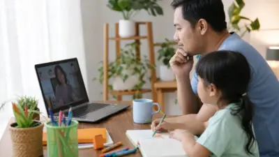 Orang tua Indonesia menonton webinar grafologi di laptop dengan buku dan tulisan tangan anak di meja dalam suasana rumah yang hangat